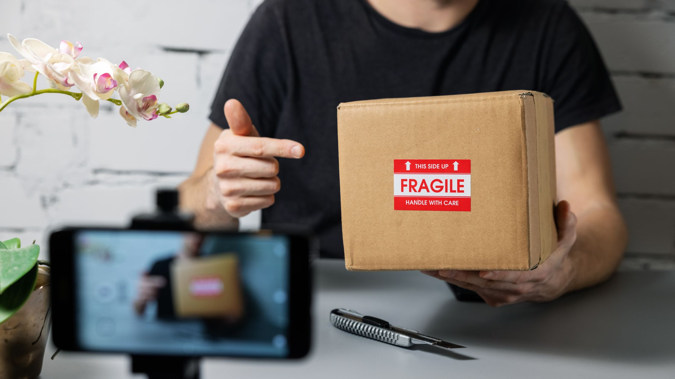 Faceless person recording a video while holding a cardboard box with a Fragile sticker - creating a social media video marketing strategy - CM2 Media.