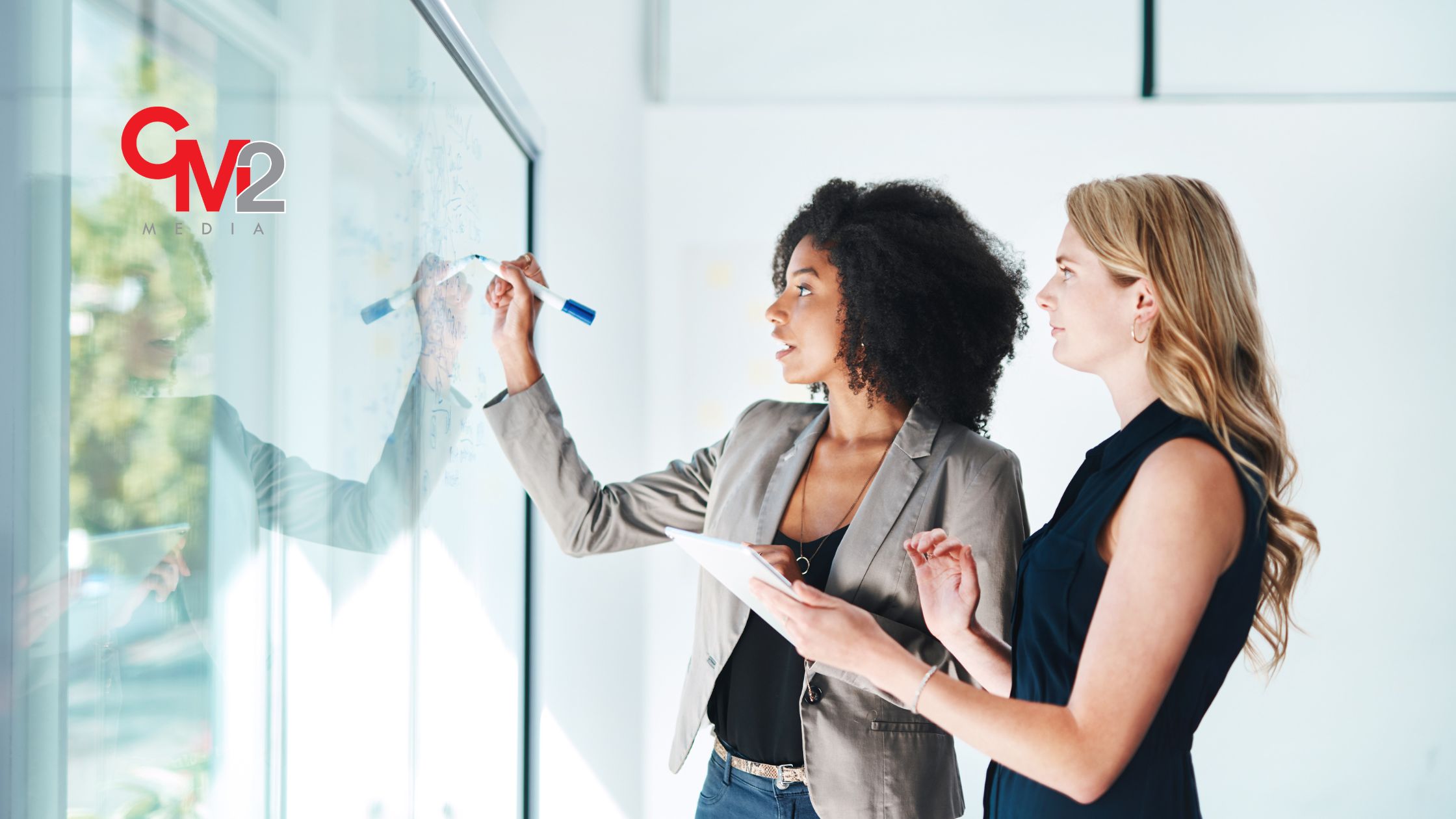 Two women using a clear board to write something - introduction to brand strategy from CM2 Media. 