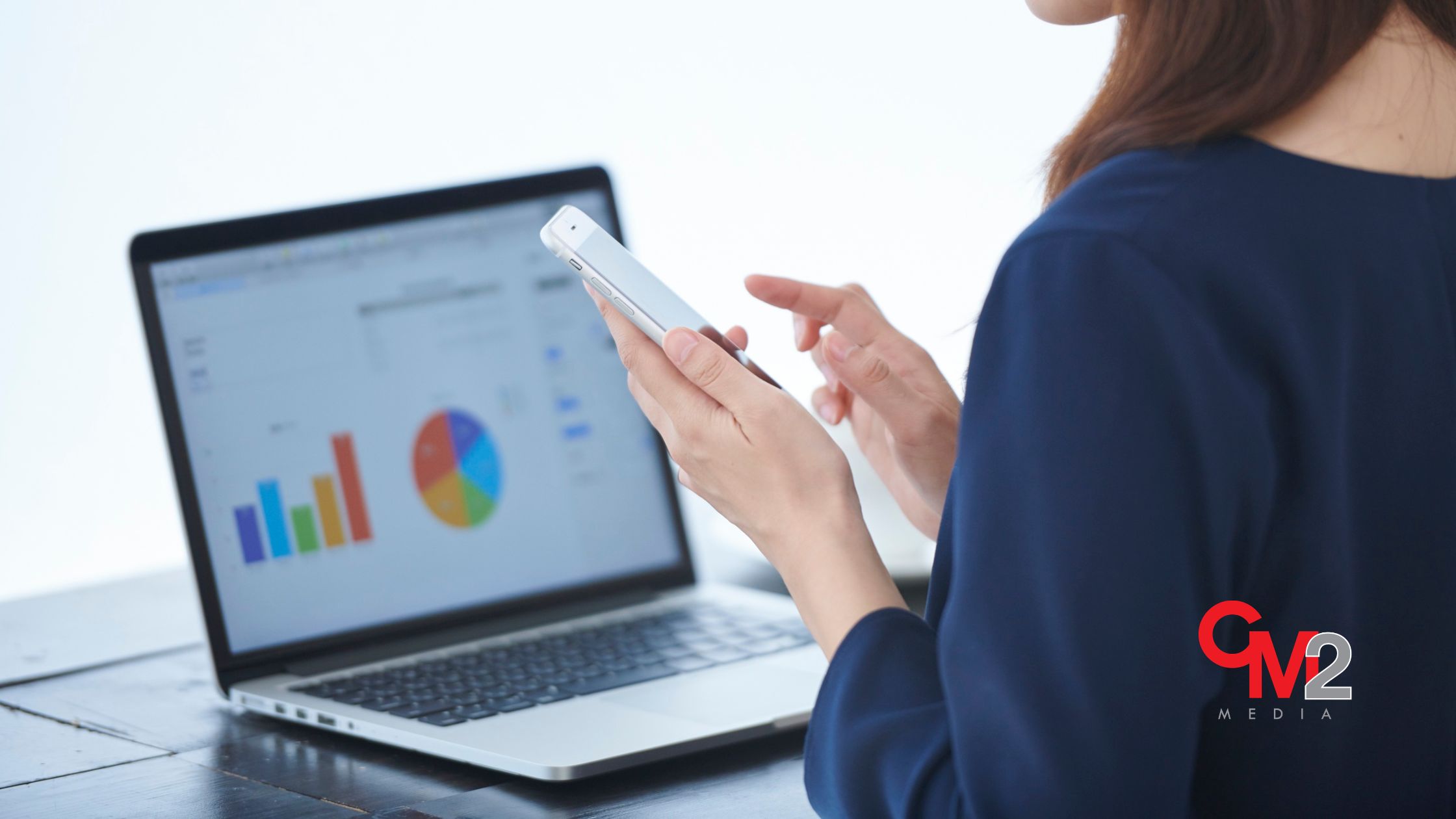 Faceless woman using a phone with a laptop - social media optimization tips from CM2 Media.